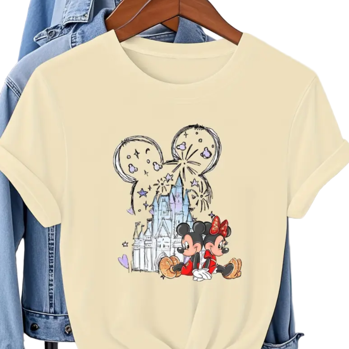 Beige t-shirt with cartoon character design on a hanger against a denim jacket background.